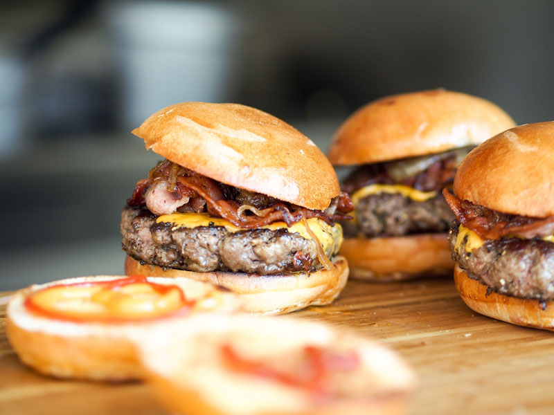 juicy burgers topped with bacon on a cutting board